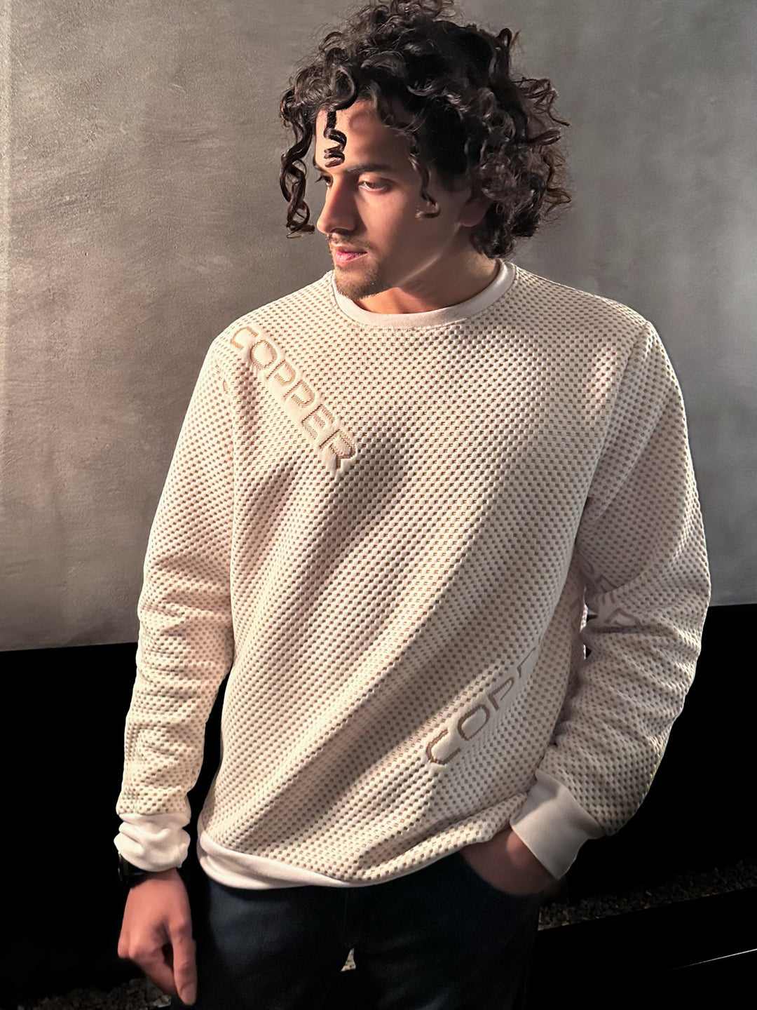 Man wearing a textured beige sweater with a brand logo against a neutral background