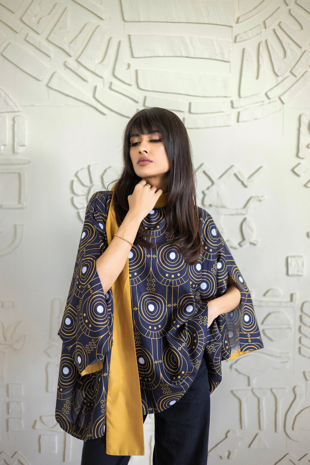 Woman wearing a patterned shawl against an abstract wall.