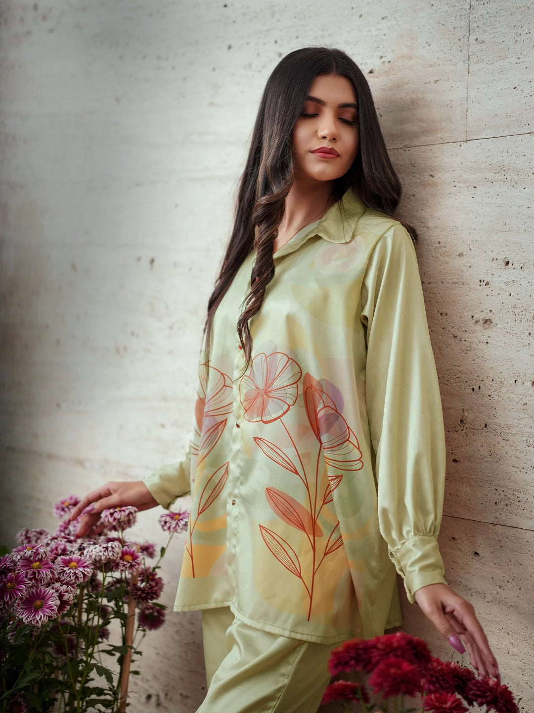 Woman wearing a light green floral shirt against a textured wall.