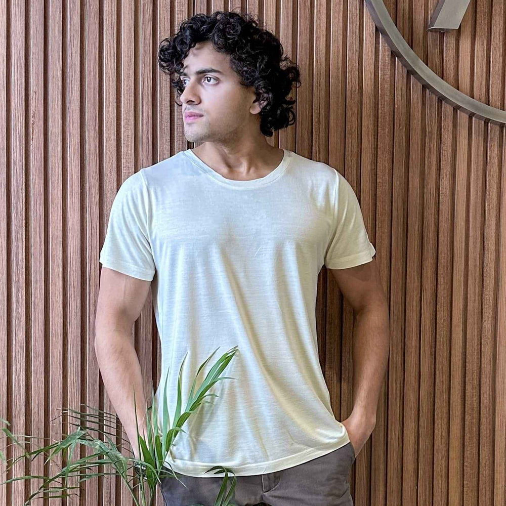 Man wearing a white t-shirt standing against a wooden wall with a plant in the foreground
