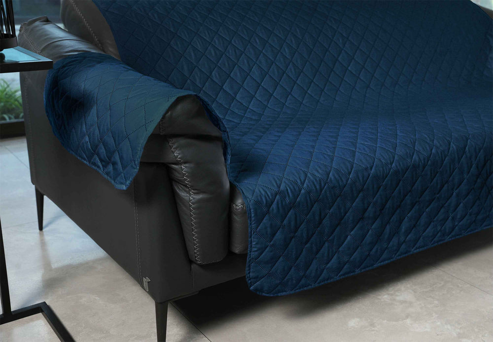 Blue quilted cover on a gray sofa in a room with a table and window.