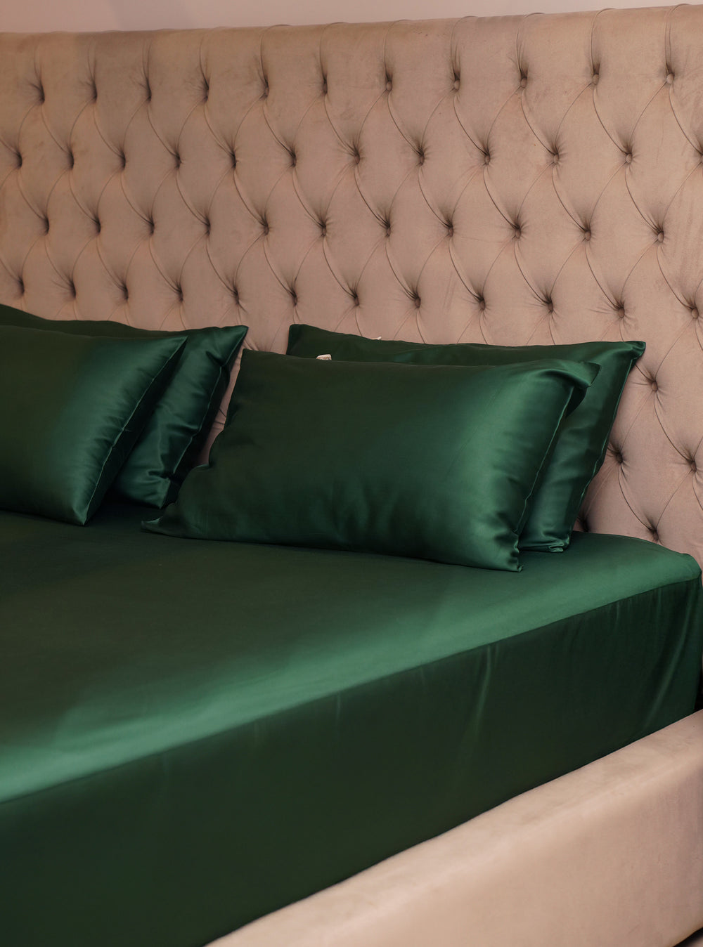 Green satin bedding set on a bed with a tufted headboard.