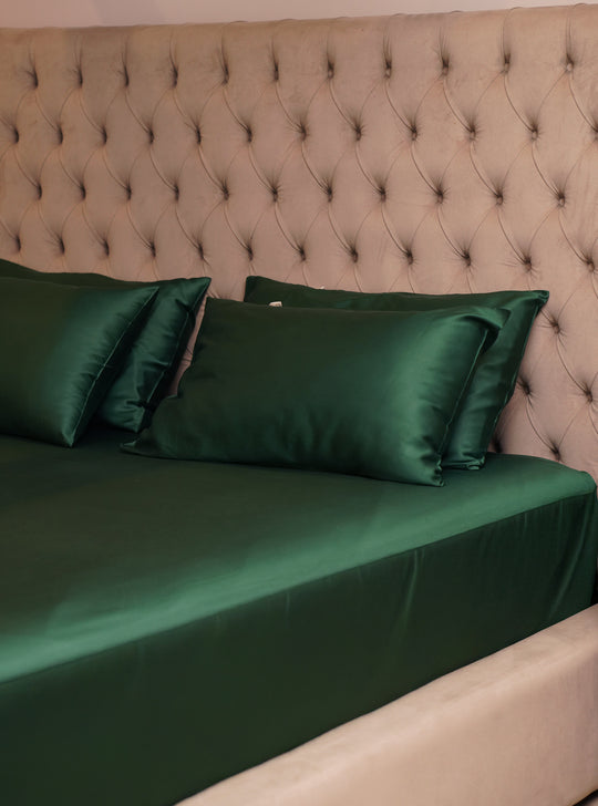 Green satin bedding set on a bed with a tufted headboard.