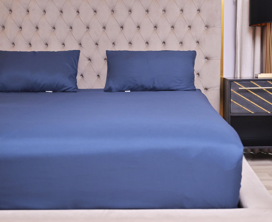 Blue bed sheets and pillows on a neatly made bed with a tufted headboard.