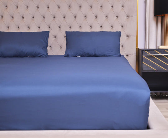 Blue bed sheets and pillows on a neatly made bed with a tufted headboard.