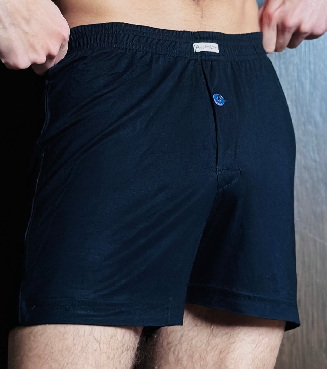 Person wearing navy blue boxer shorts with a brand logo on a wooden floor.