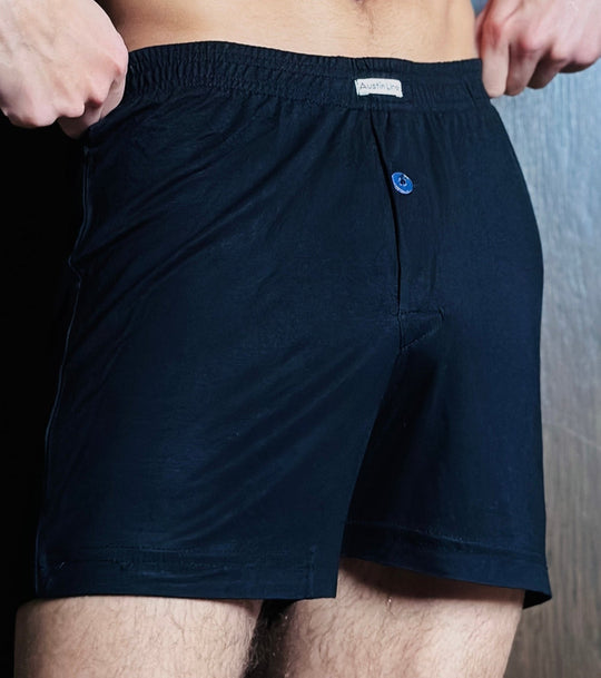 Person wearing navy blue boxer shorts with a brand logo on a wooden floor.