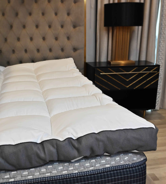 White comforter on a bed with a dark nightstand and lamp in a bedroom setting.