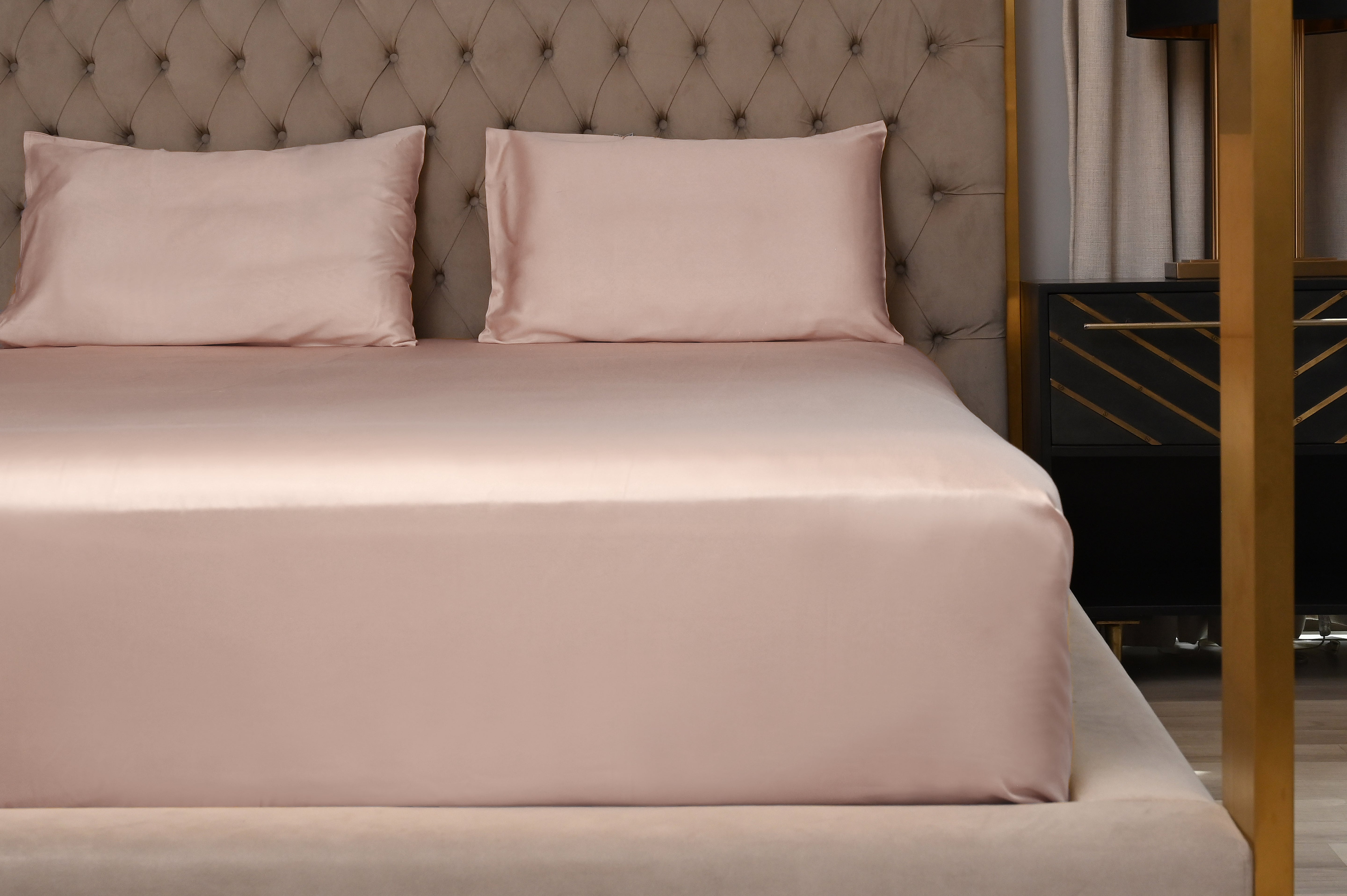 Bed with pink satin sheets and pillows against a tufted headboard.