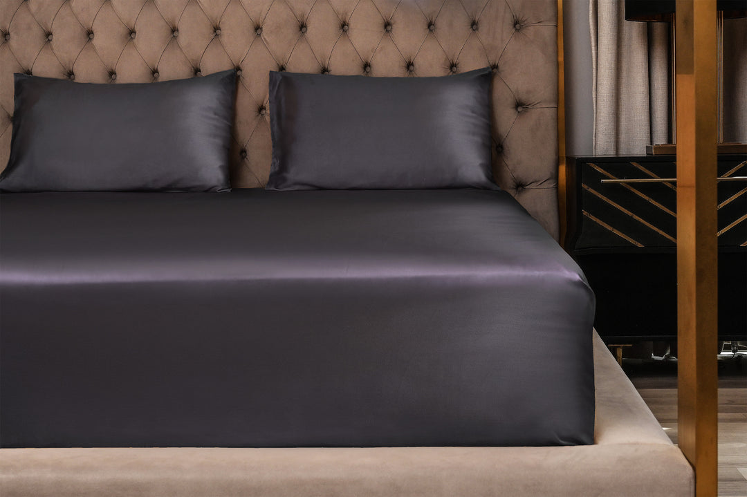 Dark purple satin sheet set on a bed with a tufted headboard.