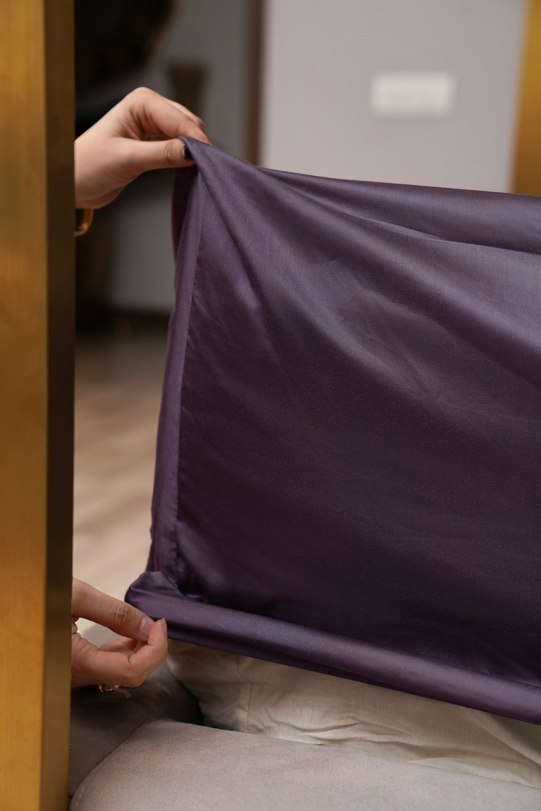 Person folding a purple fabric item in a room with wooden furniture.