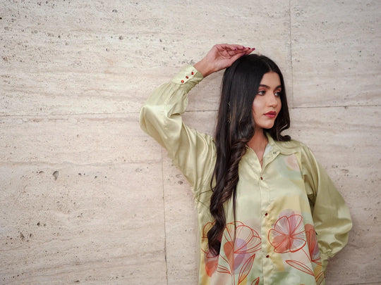 Woman wearing a light green floral blouse against a textured wall.