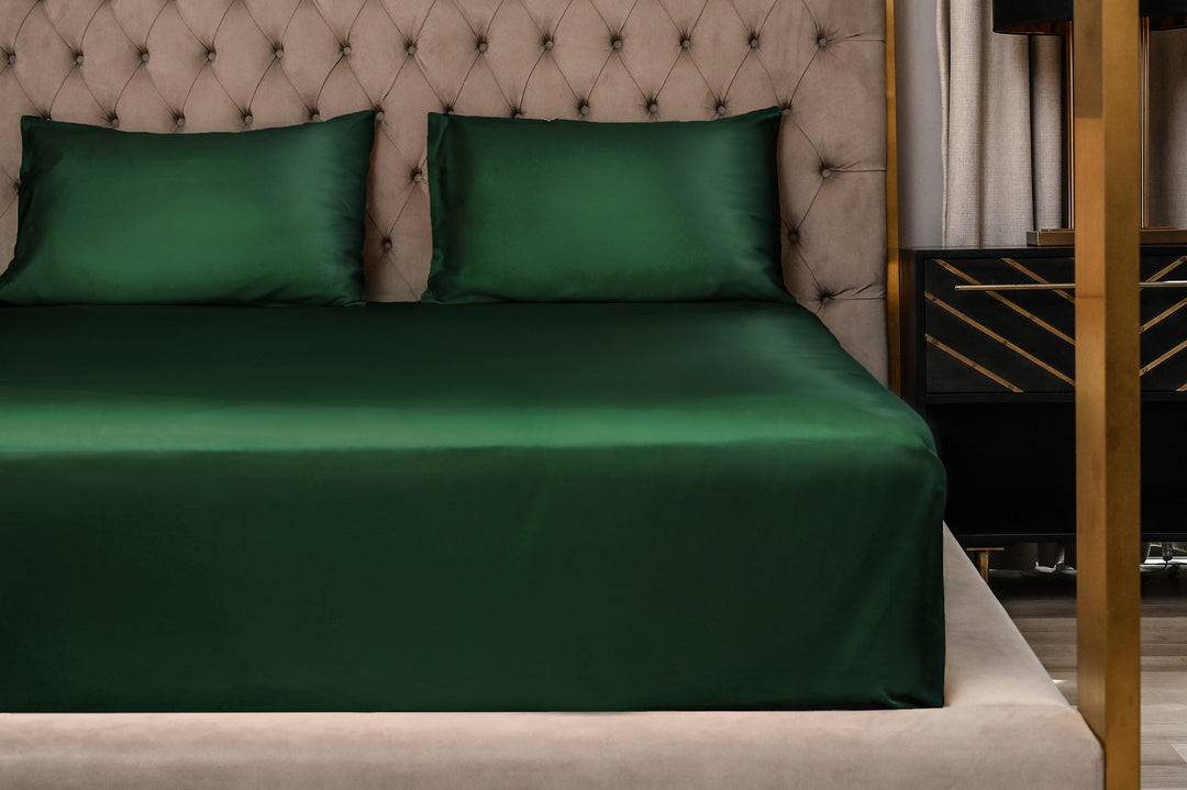 Green satin sheet set on a bed with a tufted headboard.