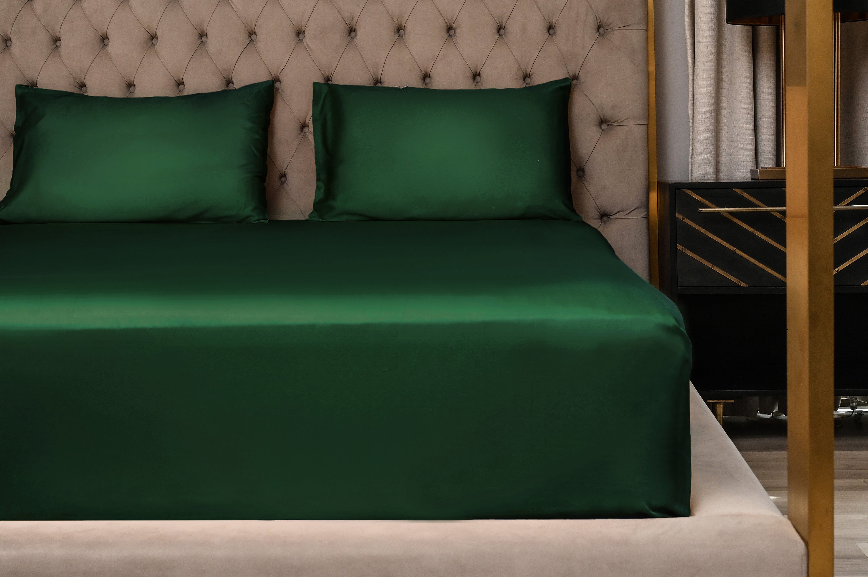 Green bed sheets on a bed with a tufted headboard and nightstand.