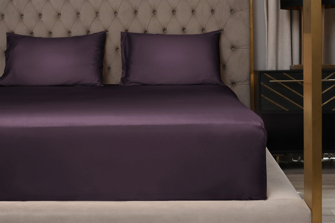 Purple bed sheets on a neatly made bed with a tufted headboard.
