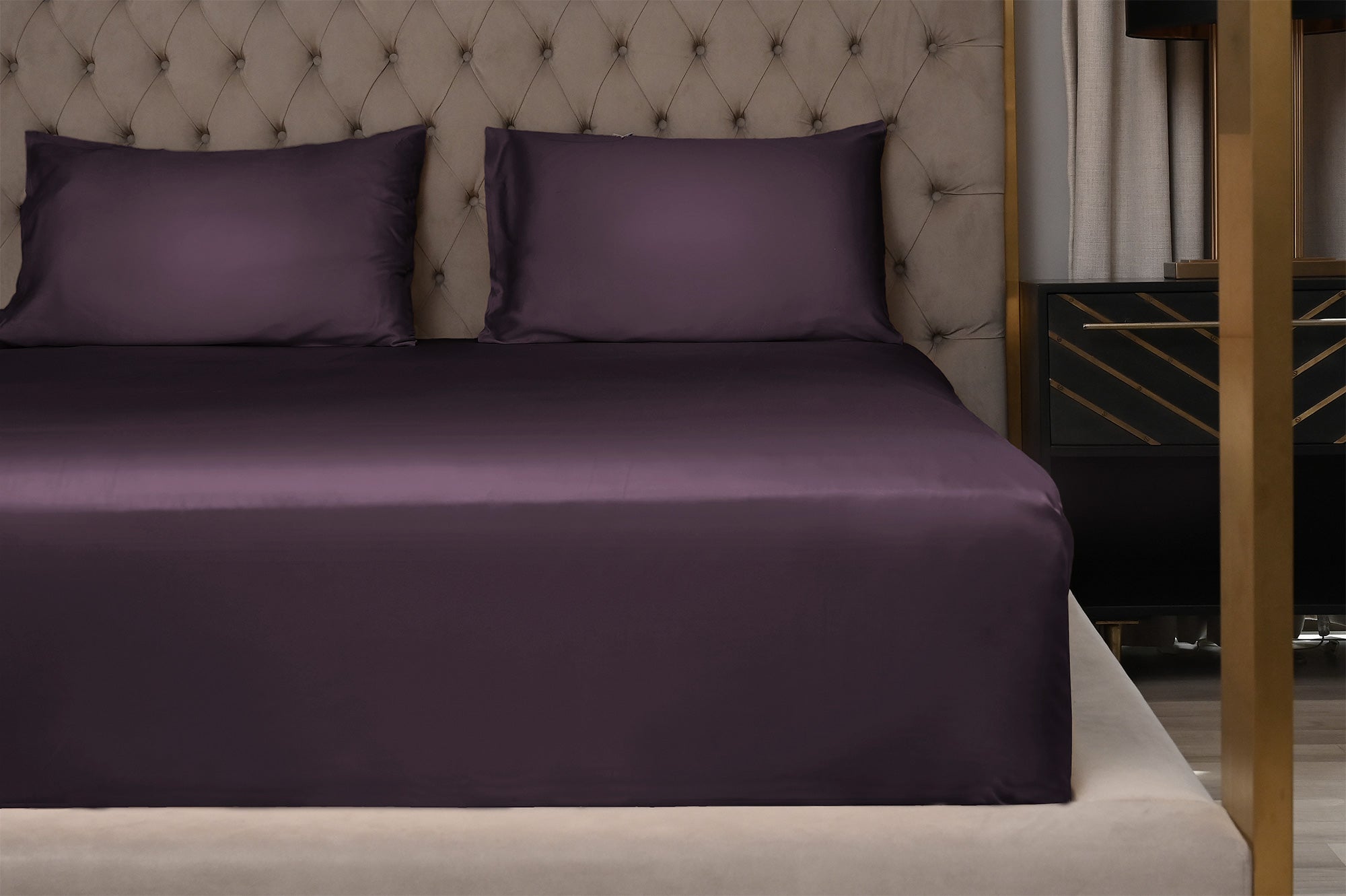 Purple bed sheets on a neatly made bed with a tufted headboard.