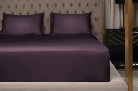 Purple bed sheets on a neatly made bed with a tufted headboard.